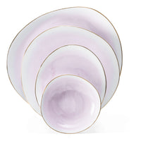 The Galette Dinnerware set by Molecot includes four pastel lavender plates and bowls with irregular round shapes, hand-painted porcelain, subtle gold rims, and a glossy finish—each piece stacks neatly inside the next.