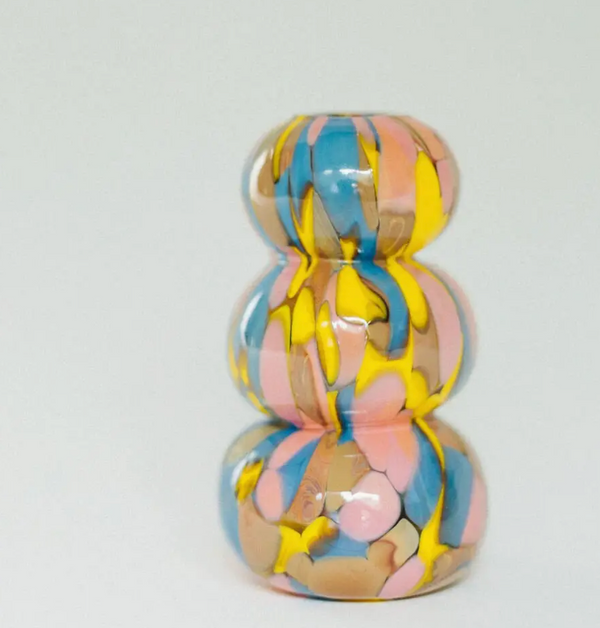 Introducing the Jelly Baby Mini Vase Collection by Maria Ida Designs—a handmade art glass vase featuring a glossy, three-tiered abstract form with swirled patterns of yellow, blue, pink, and beige. Set against a plain light gray background, this unique piece makes for truly distinctive home decor.