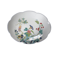 The Royal Limoges Nymphea Paradis Bleu is an oval, white porcelain dish with scalloped edges, decorated inside with a vibrant floral and vine pattern in green, pink, yellow, blue, and red.
