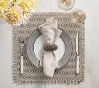 A refined table setting featuring a textured placemat, ornate plate, neatly folded beige napkin in the Kim Seybert Demilune Napkin Ring Silver Set of 4, with silverware, wine glass, and pale yellow flowers on a white surface.