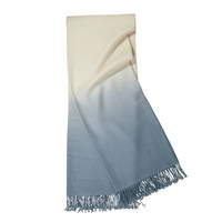 The Johanna Howard Dip Dye Throw features a gradient ombré design that transitions from cream to light blue, finished with stylish fringed edges.