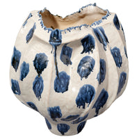 The Moncler Blue Vase by Jamie Young is a white ceramic piece with an uneven, jagged rim, featuring large blue reactive glaze spots and drips for a handcrafted, organic look.