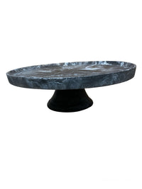The Nashi Home Swirl Resin Classic Footed Cake Plate features a round, dark design with a wide, flat surface and sturdy base—ideal as a food-safe tray for cakes or displaying resin decor against a plain white background.