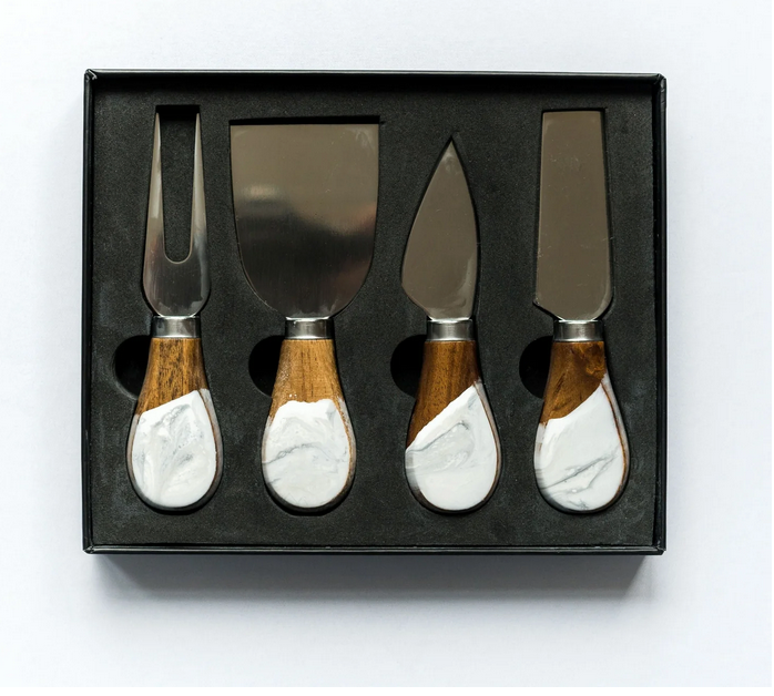 Elevate your cheese board with the Lynn & Liana Serveware Painted Cheese Knives s/4 - White Marble, featuring four stainless steel knives with marble design and wood handles, all in a sleek black box with foam insert.