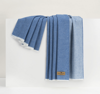 A folded denim blue Lands Downunder Aspen Reversible Throw with frayed edges rests on a white surface. A brown tag is attached, highlighting this soft, cozy blanket's stylish and versatile design.