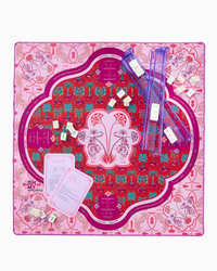 Oh My Mahjong’s Mahjong Mats feature a pink, red, and purple neoprene game mat with decorative motifs and symmetrical patterns, plus rectangular cards, sliding rulers, and small wrapped tokens for a colorful gaming experience.