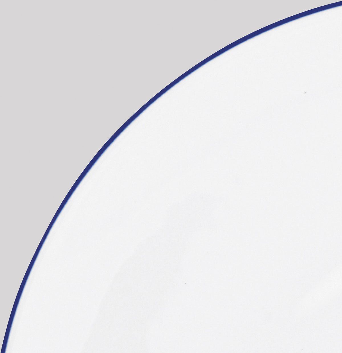 A close-up shows the Raynaud Monceau Bleu Outremer Dinnerware—a white ceramic plate with a thin ultramarine blue rim—set against a light gray background, with only part of the plate visible.
