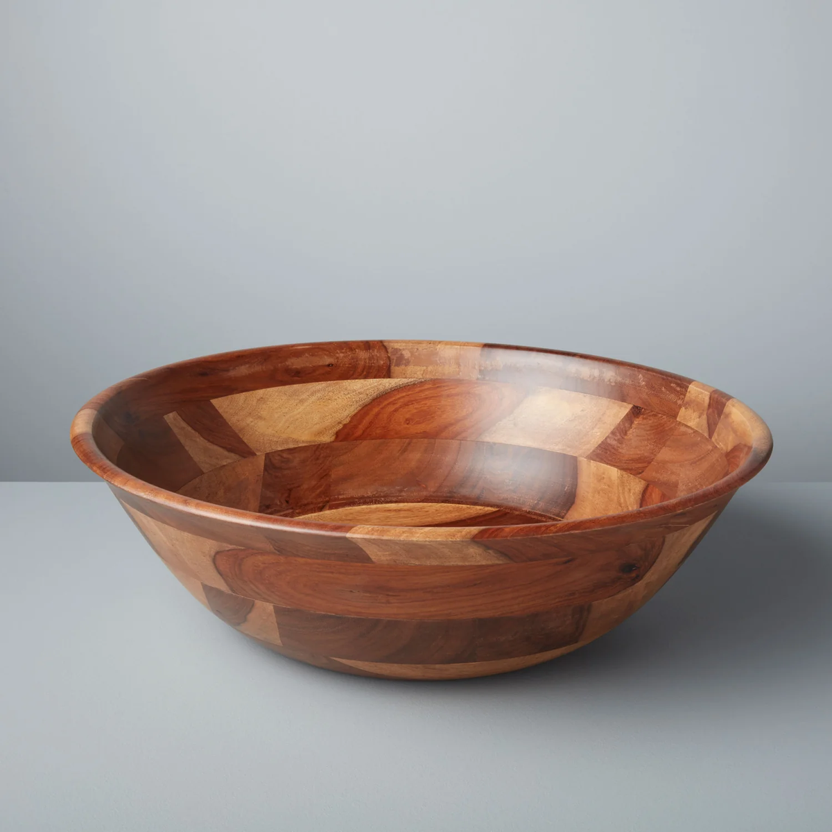 The Be Home Rosewood Bowl - XLarge, featuring a smooth, patchwork design and made from sustainably sourced wood, rests on a light gray surface with a matching background.