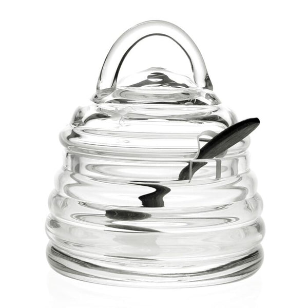 The William Yeoward Honeybee Honey Jar & Spoon is a handmade crystal beehive-shaped jar with lid, featuring a slot for the included matching spoon that rests inside.