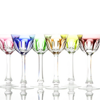 Six Moser Lady Hamilton White Wine Glasses with long stems are arranged in a row, each tinted blue, purple, green, yellow, orange, or red—vivid colors on classic crystal—set against a white background with reflections below.