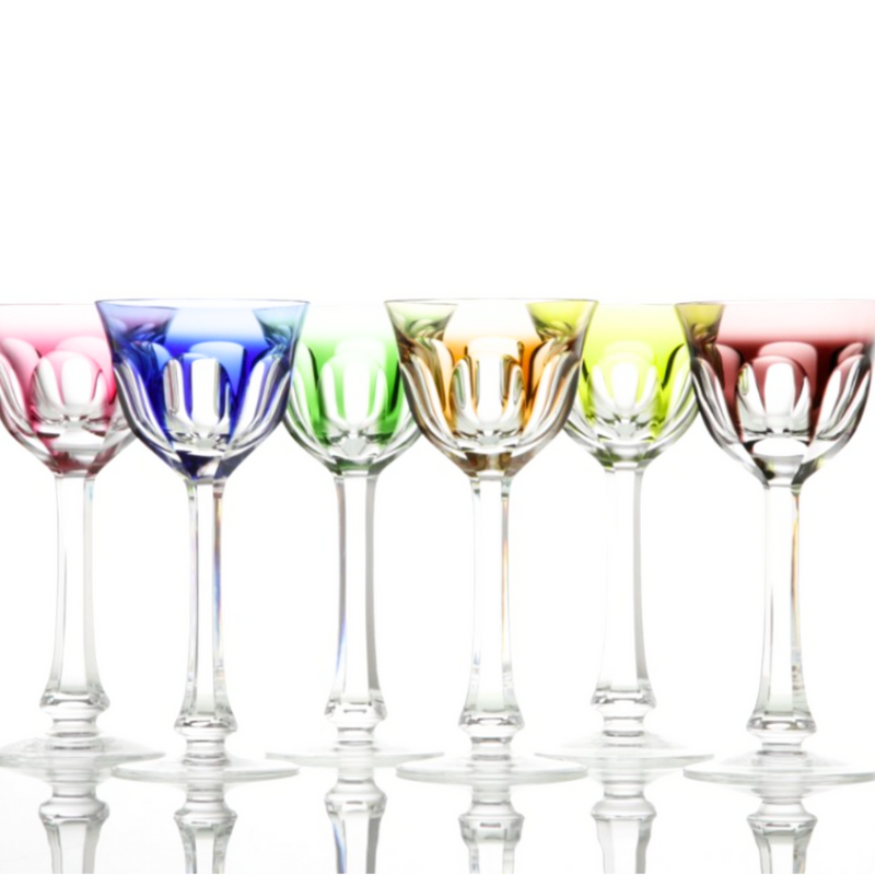 Six Moser Lady Hamilton White Wine Glasses with long stems are arranged in a row, each tinted blue, purple, green, yellow, orange, or red—vivid colors on classic crystal—set against a white background with reflections below.
