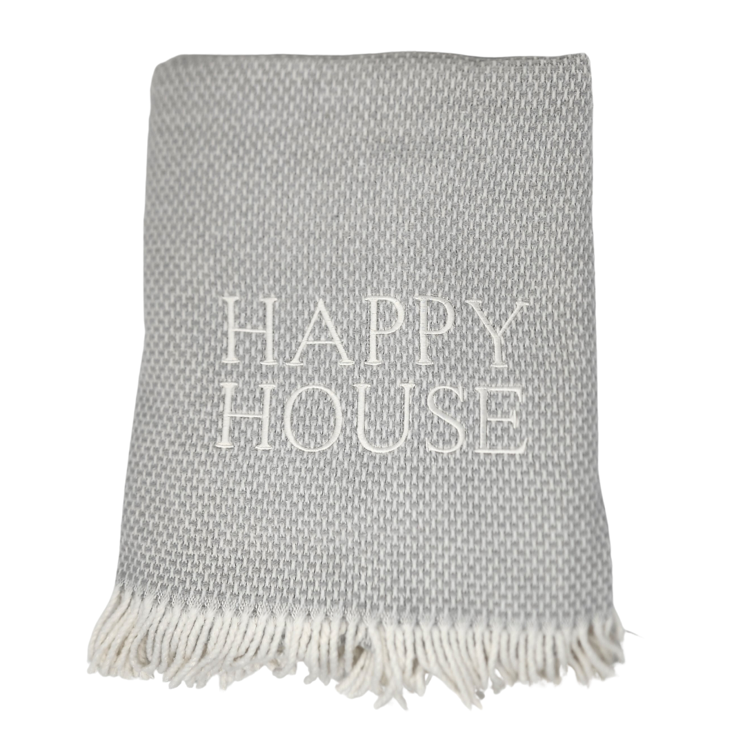 The Happy House Throw by A Soft Idea is a folded gray woven blanket with white fringed edges and "HAPPY HOUSE" embroidered in large white letters. This home exclusive throw is machine washable for easy care.