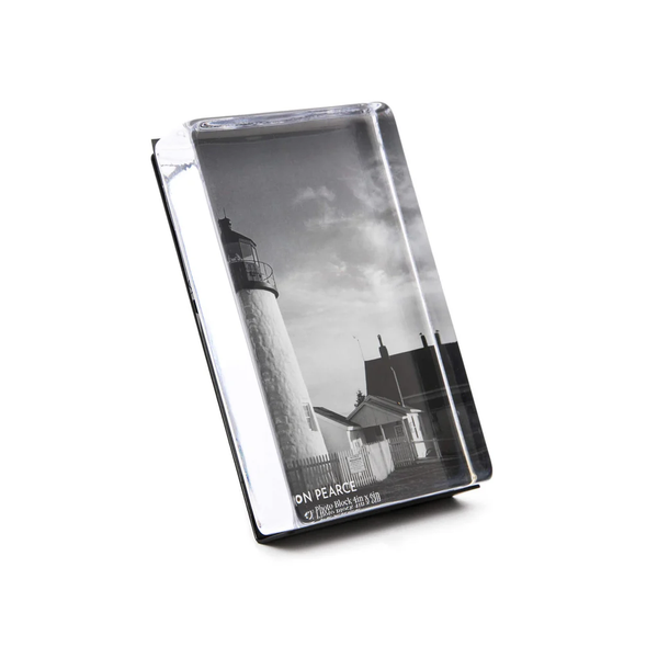 The Simon Pearce Woodbury Photo Block Vertical is a rectangular, handcrafted, lead-free glass plaque featuring a black-and-white lighthouse image under clouds. The angled design displays "ON PEACE" and other small text at the bottom.
