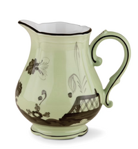 The Oriente Italiano Dinnerware Bario by Ginori 1735 is a pale green ceramic pitcher with a curved handle, black chinoiserie floral and geometric designs, white interior, and scalloped base, shown on a white background.