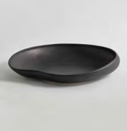 The Tefra Bowl by Greg Natale is a black, shallow, matte ceramic piece with an irregular organic form and subtle textured glaze, styled on a light gray background—ideal for modern interiors.