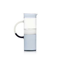 The Ichendorf Milano Tequila Sunrise Cylinder Pitcher, made from clear glass with a large curved handle and light blue base, is the perfect stylish cocktail pitcher for your barware setup. Shown on a plain white background.