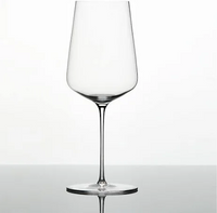 A clear, empty Zalto Universal Glass by Grand Cru Selections / Zalto, made from lead-free crystal with a long stem and wide bowl, rests on a reflective surface against a plain white background.
