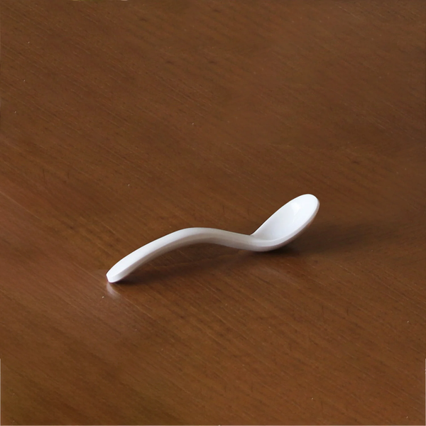 The Beatriz Ball Vida Havana Spoon - Mini, a single white melamine serving spoon with a curved handle, BPA free and dishwasher safe, sits on a wooden surface.