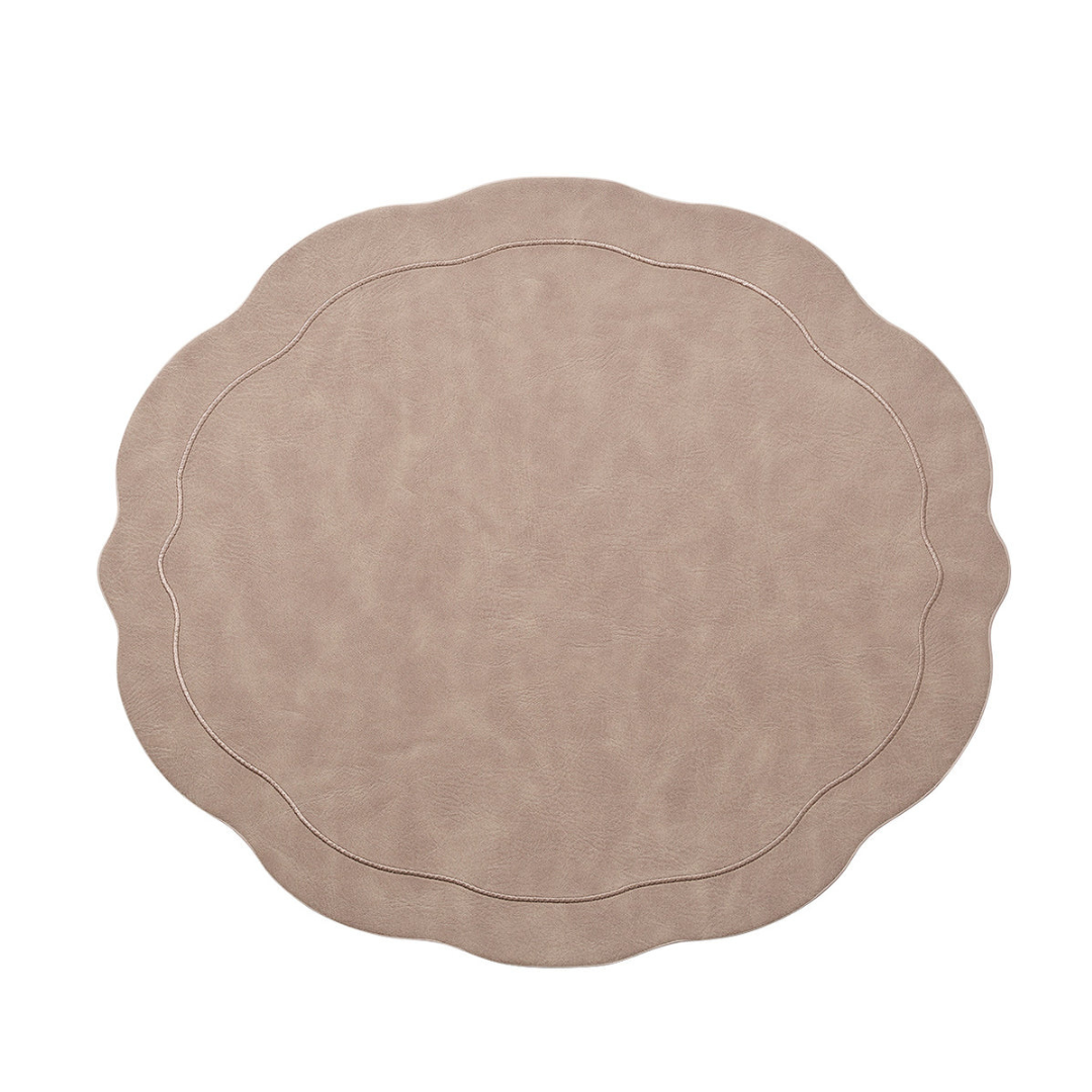 The Kim Seybert Tailored Placemat Taupe Set of 4 features a beige faux leather design with wavy scalloped edges, subtle stitched borders, and a soft, textured surface, shown on a white background.