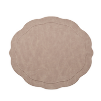 The Kim Seybert Tailored Placemat Taupe Set of 4 features a beige faux leather design with wavy scalloped edges, subtle stitched borders, and a soft, textured surface, shown on a white background.