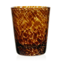 The Vanessa Drinkware Tortoise by William Yeoward is a handcrafted crystal tumbler with an amber and brown tortoiseshell pattern, marbled texture, glossy finish, and cylindrical shape with a slightly wider rim.