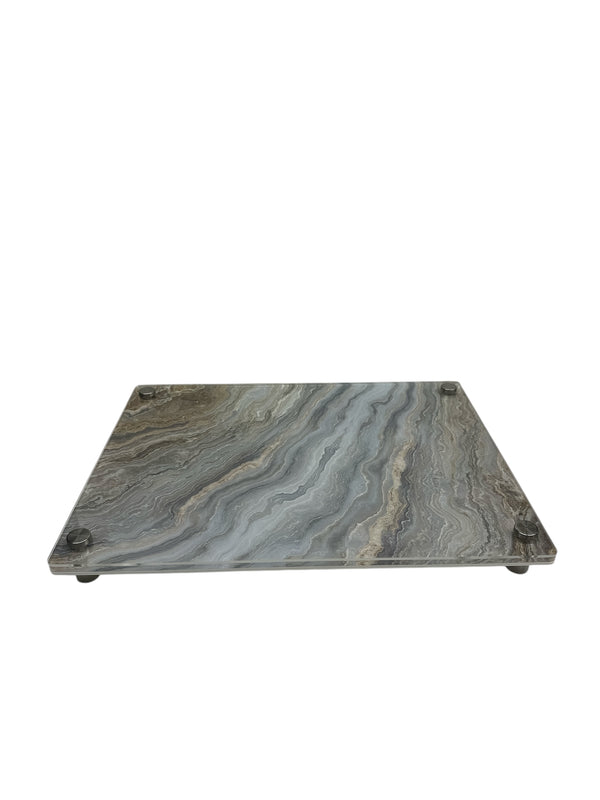 The Eye Candy Raised Challah Board features a rectangular glass design with a grey marble slice pattern and is supported by four silver feet.