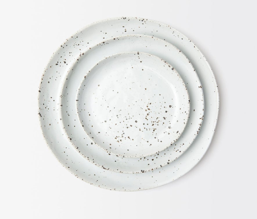 Four round, white ceramic plates with brown speckles from Blue Pheasant’s Marcus Dinnerware - White Salt Glaze set are stacked against a plain white background, highlighting their artisanal craftsmanship.