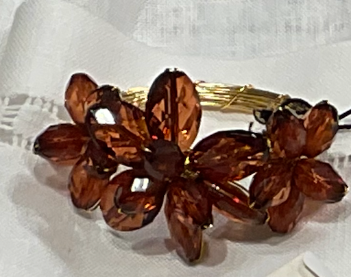 The Tiara Beaded Napkin Rings Set of 4 by Deborah Rhodes features two large, faceted brownish-red bead floral designs, beautifully displayed on a white fabric background.
