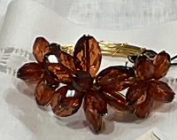 The Tiara Beaded Napkin Rings Set of 4 by Deborah Rhodes features two large, faceted brownish-red bead floral designs, beautifully displayed on a white fabric background.