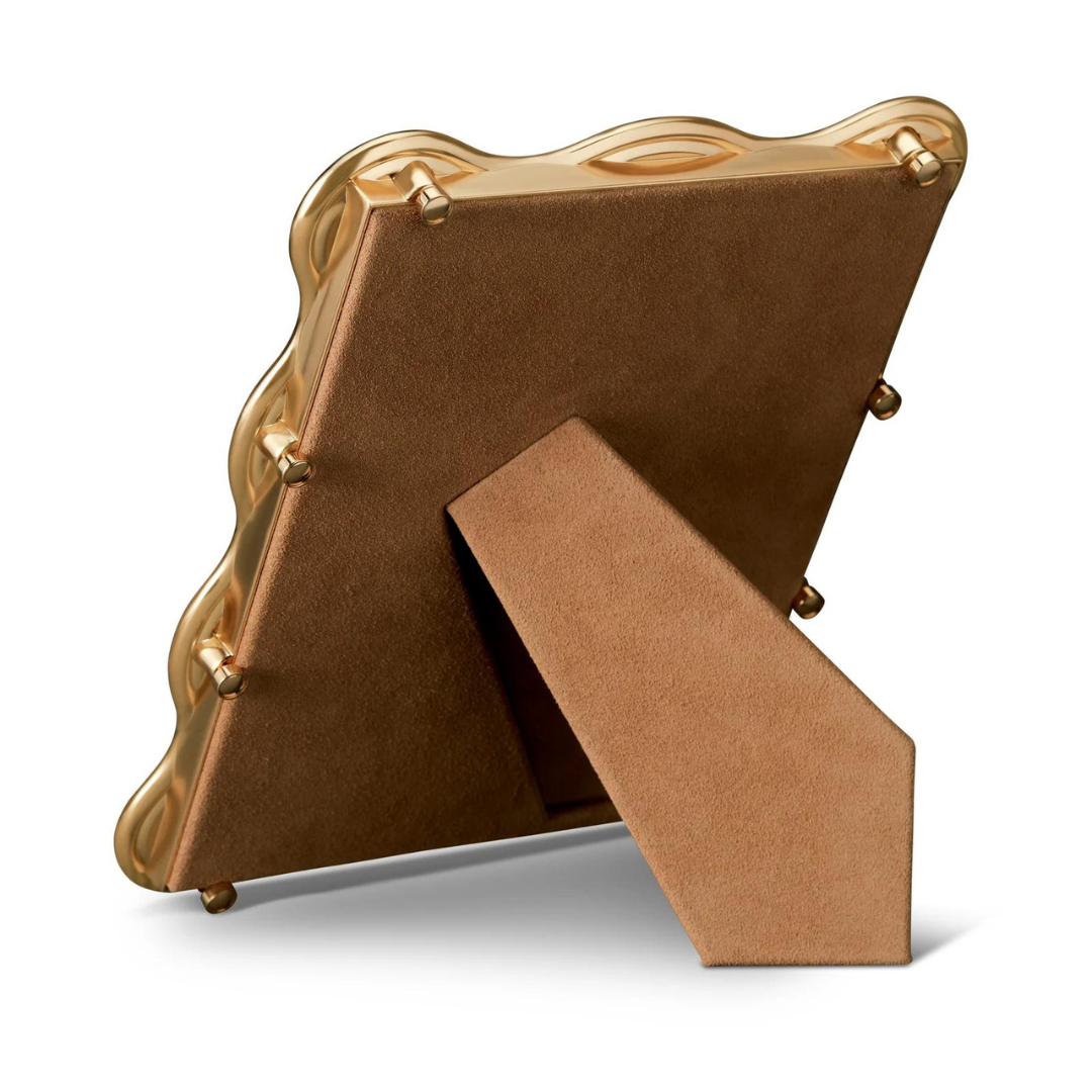 The L'Objet Ripple Frame Gold features a modern wavy-edge design. Its back and stand are covered in brown suede-like material, letting the frame stand upright on flat surfaces.