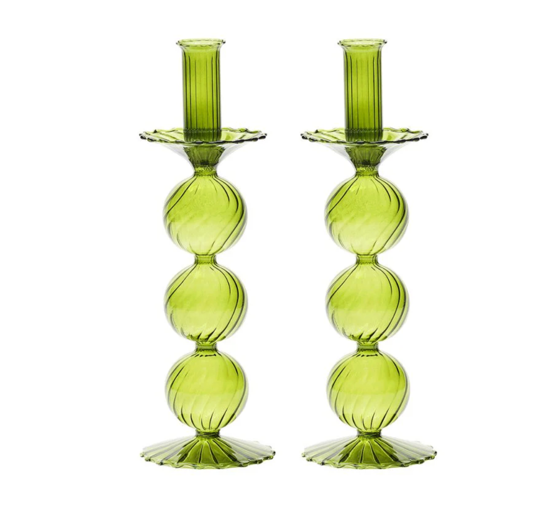 The Iris Candlestick Holder Set of 2 by Kim Seybert features two green glass holders, expertly crafted from hand-blown glass with a vertically stacked, round bubble design and elegant scalloped bases, displayed side by side on a white background.