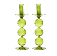The Iris Candlestick Holder Set of 2 by Kim Seybert features two green glass holders, expertly crafted from hand-blown glass with a vertically stacked, round bubble design and elegant scalloped bases, displayed side by side on a white background.
