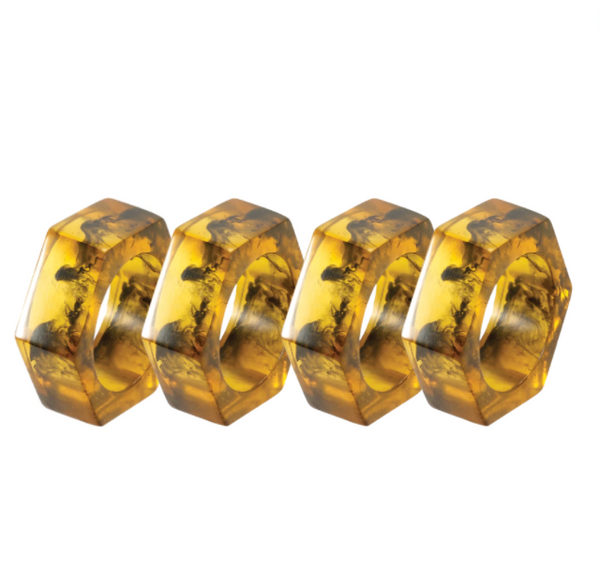 The Piper Napkin Rings, Tortoise Set of 4 by Bodrum are arranged in a row on a white background, highlighting the contemporary appeal of these modern napkin rings with their hexagonal shape and dark tortoise-patterned inclusions.