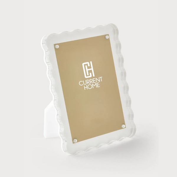 The Waverly Frame White by Tizo is a clear lucite picture frame with wavy, scalloped edges and gold backing, featuring the CH Current Home logo—an elegant choice for modern décor.