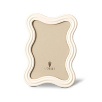 The Ripple Enamel Frame White by L'Objet features a wavy white enamel design, handcrafted in Portugal, with a tan backing and the L'Objet logo at the bottom.