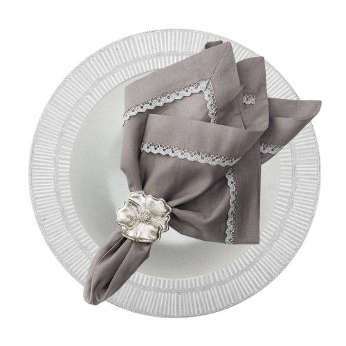 A gray linen napkin with lace trim, held by a silver floral napkin ring and placed on a white plate with a striped rim, rests atop the elegant Nomi K Shine Round White Placemat.