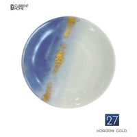 A round porcelain dinnerware plate by Marie Daâge, featuring a blue and white gradient with a gold vertical streak, hand-painted and named Horizon Gold. The Current Home logo appears at the top left.