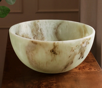 The Beatriz Ball Resin Giada Bowl Jade Swirl - Large features unique beige and brown marbling with jade-inspired swirls and sits on a wooden surface in a softly lit room.