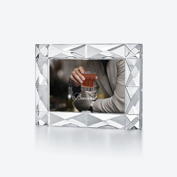 The Baccarat Louxor Frame, crafted in France with a diamond-cut pattern, showcases a man in a blazer holding a glass of amber liquid—a stylish decorative accent for any space.