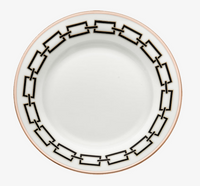 The Catene Nero Dinnerware by Ginori 1735 features a white ceramic plate adorned with a geometric black border pattern around the rim and finished with a thin gold edge.