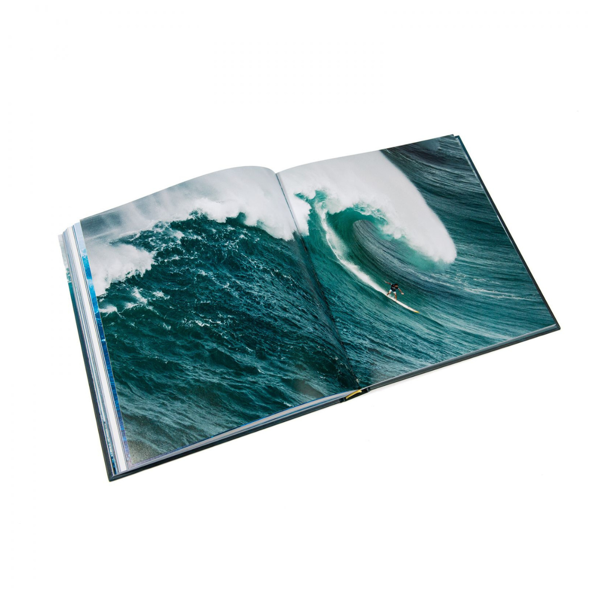 The Rizzoli "Big Wave Surfer" book features a striking image of a surfer riding a massive, curling ocean wave—an impressive showcase of surfing photography.