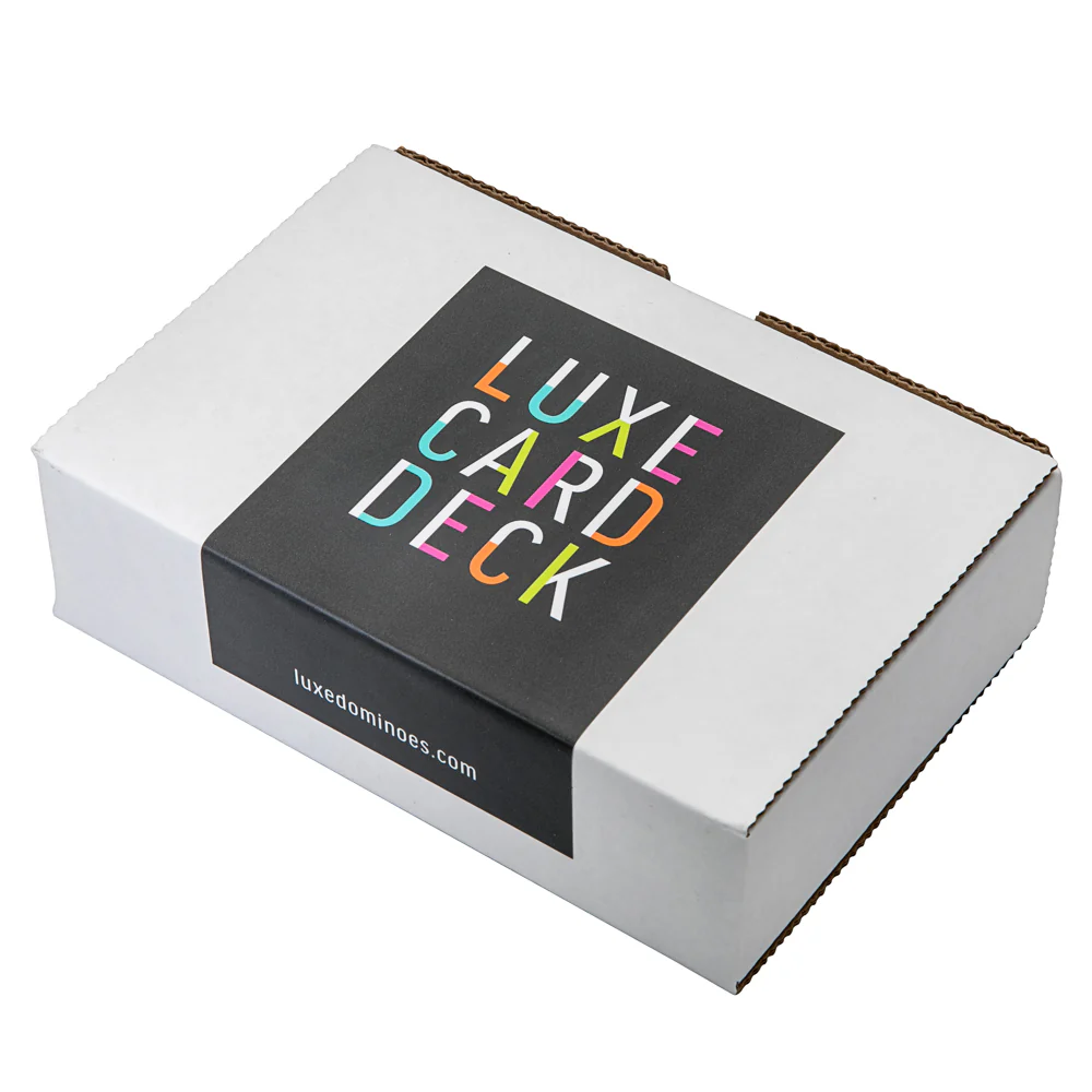 A transparent La Pinta Card Deck from Luxe Dominoes is shown in a white box with a black "LUXE CARD DECK" label in colorful letters and luxeominoes.com printed below, placed closed on a white background.