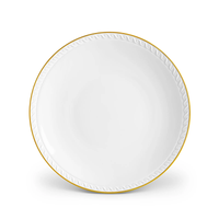 The L’Objet Neptune Gold dinnerware plate is crafted from fine white porcelain with a 24k gold rim and a textured wave pattern along the edge, displayed against a white background.