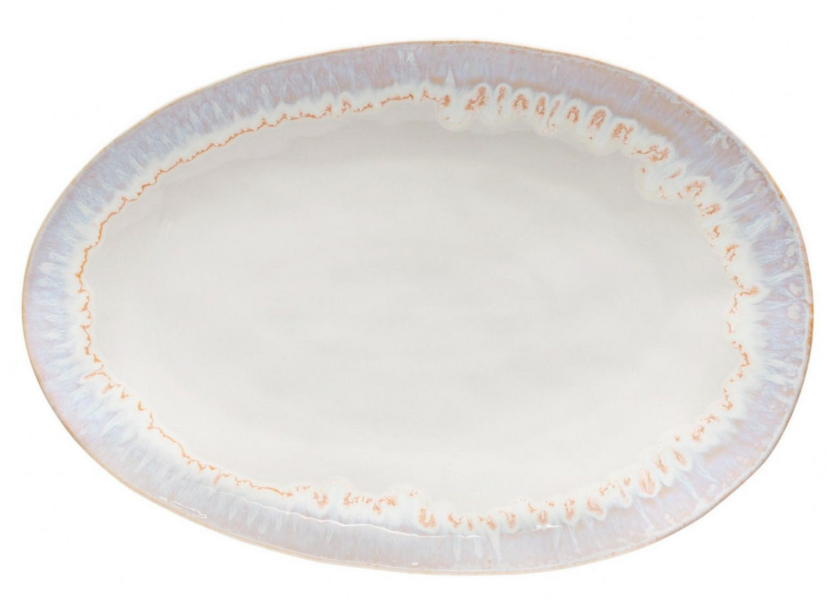 The Brisa Sal Dinnerware by Casafina/Costa Nova is an oval stoneware plate with a glossy off-white center and light blue and beige decorative rim, inspired by the Algarve coast. Made in Portugal, it offers a simple, elegant design.