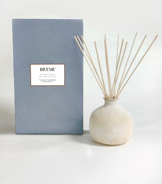 The Blueme Spiritual Diffuser is a minimalist ceramic set with a round, pale vase and reed sticks, presented beside its light blue box. It offers therapeutic aroma wellness fragrances against a clean white background.