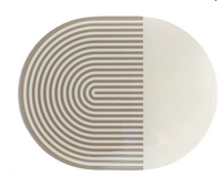 The Von Gern Home Stripes & Solids Lacquer Placemat Set of 4 features oval placemats with a bold beige and white color-blocked design—half with curved beige stripes, half solid white—for a modern table setting.