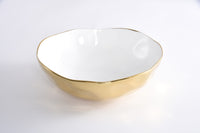 The Moonlight Bowl by PAMPA BAY is a glossy white ceramic bowl with a gold titanium rim, an uneven edge, and a metallic gold exterior. Oven safe, it’s ideal for elegant porcelain serveware displays against a plain white background.