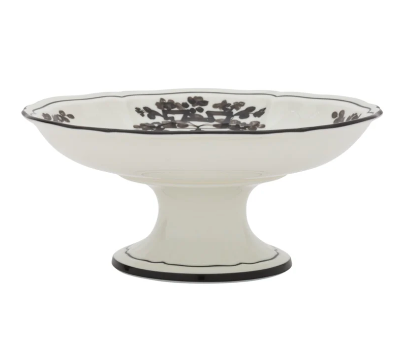 The Oriente Italiano Dinnerware Albus by Ginori 1735 is a white ceramic pedestal bowl, handcrafted in Italy, with black floral designs inside and a scalloped rim.