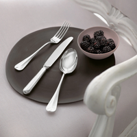 A fork, knife, and spoon from the Sambonet Baguette Stainless Steel 5PPS set are placed on a dark plate beside a small bowl of blackberries.