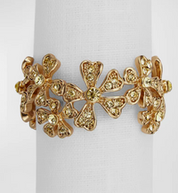 A 24K gold-plated floral bracelet with yellow gems and heart-shaped petals, displayed on a white stand. Ideal for gifting or to pair with L'Objet Garland Napkin Jewels Gold Set of 4.